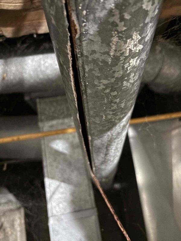 Inspected water heater requiring daily relighting and discovered significant vertical crack in exhaust vent pipe. Observed extensive cobweb accumulation throughout system indicating lack of maintenance. Recommended replacement of damaged vent pipe to prevent dangerous exhaust gas leakage and ensure proper draft for consistent pilot light operation.