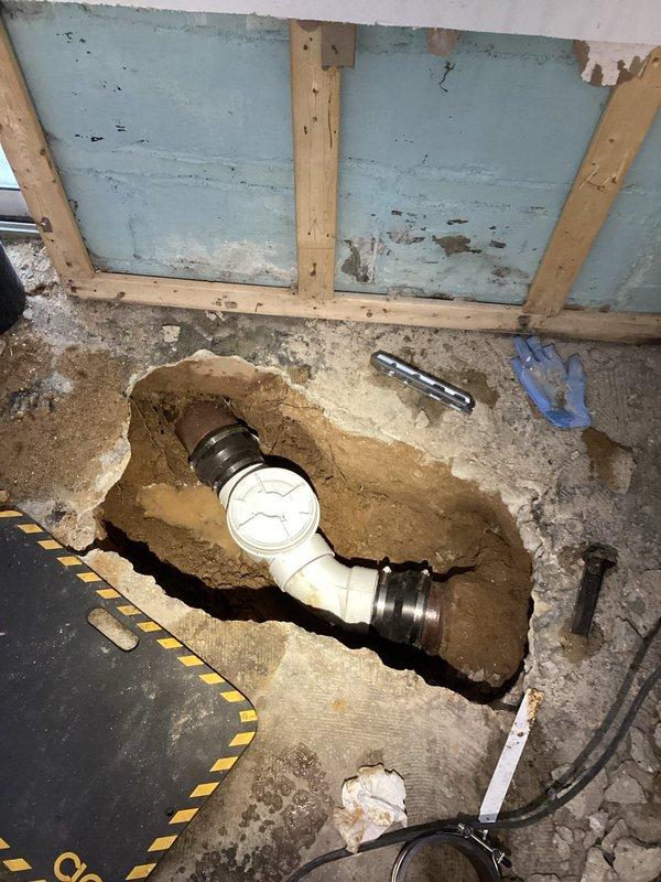 Successfully installed a backwater valve after excavating through concrete floor to access main drain line. Exposed and prepared existing plumbing connections, ensuring proper fit and alignment of the new valve. Work addressed previous water damage issues as evidenced by wet concrete and standing water around drain opening.
