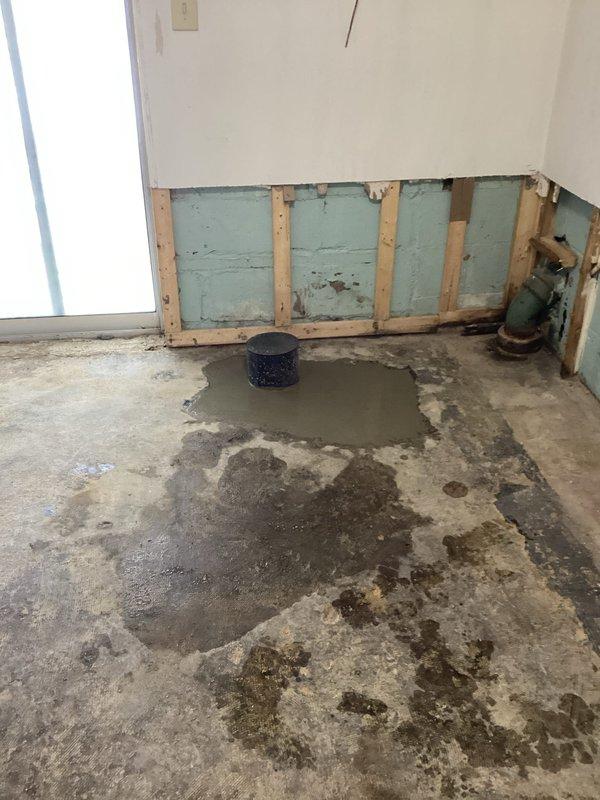 Successfully installed a backwater valve after excavating through concrete floor to access main drain line. Exposed and prepared existing plumbing connections, ensuring proper fit and alignment of the new valve. Work addressed previous water damage issues as evidenced by wet concrete and standing water around drain opening.