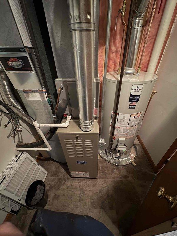 Completed installation of new Carrier furnace and water heater in residential mechanical room. System includes proper ductwork connections with galvanized metal venting, PVC piping, and all required safety components. Both units are functioning properly with no issues observed during final inspection; customer financing is pending.