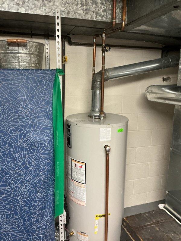 Responded to water leak complaint at water heater base. Inspected cylindrical water heater installed in basement/utility room with copper plumbing connections and metal vent piping. Identified and resolved leak source, ensuring proper operation of the residential hot water system.