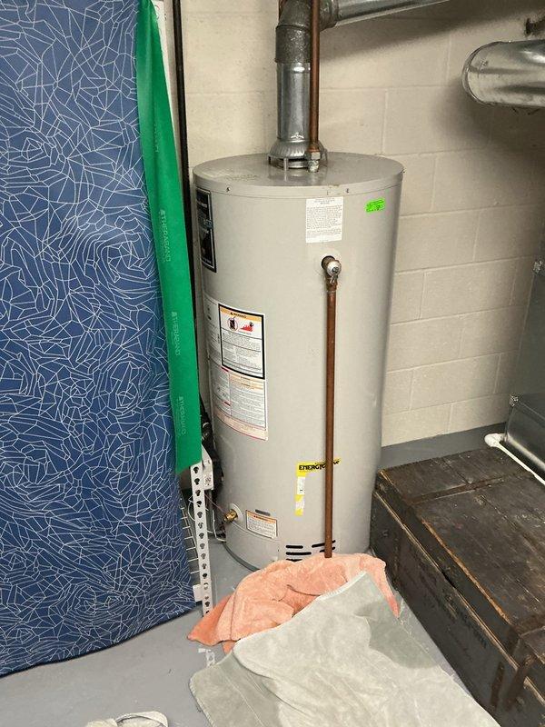 Responded to water leak complaint at water heater base. Inspected cylindrical water heater installed in basement/utility room with copper plumbing connections and metal vent piping. Identified and resolved leak source, ensuring proper operation of the residential hot water system.