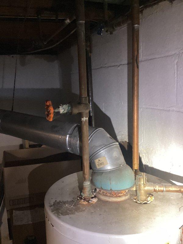 Conducted a water heater replacement estimate in basement utility area. Existing unit shows significant corrosion and mineral buildup around plumbing connections, particularly at the copper supply lines and metal vent pipe connections. Documented current installation configuration with proper photos to ensure accurate quote for replacement system.