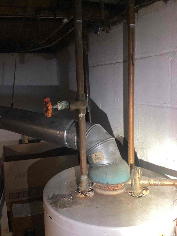 Conducted a water heater replacement estimate in basement utility area. Existing unit shows significant corrosion and mineral buildup around plumbing connections, particularly at the copper supply lines and metal vent pipe connections. Documented current installation configuration with proper photos to ensure accurate quote for replacement system.