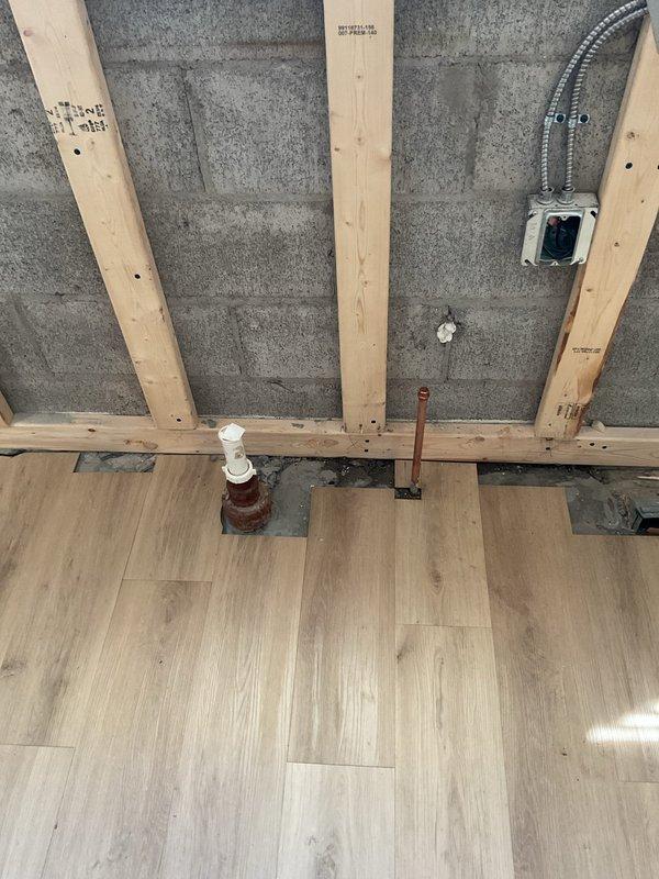 Completed kitchen plumbing rough-in work for renovation project, installing copper and PVC supply lines through floor. Positioned and secured piping according to project specifications, ensuring proper placement for future fixture installation in the concrete block wall construction area.