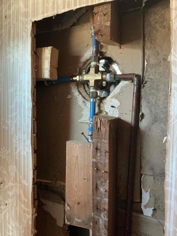 Responded to service call for low hot water pressure in tub/shower fixture. Accessed wall cavity behind shower controls to inspect plumbing system, revealing a malfunctioning four-way diverter valve with blue PEX supply lines and copper pipe connections. Successfully replaced the faulty valve assembly, restoring proper hot water pressure to the shower system.