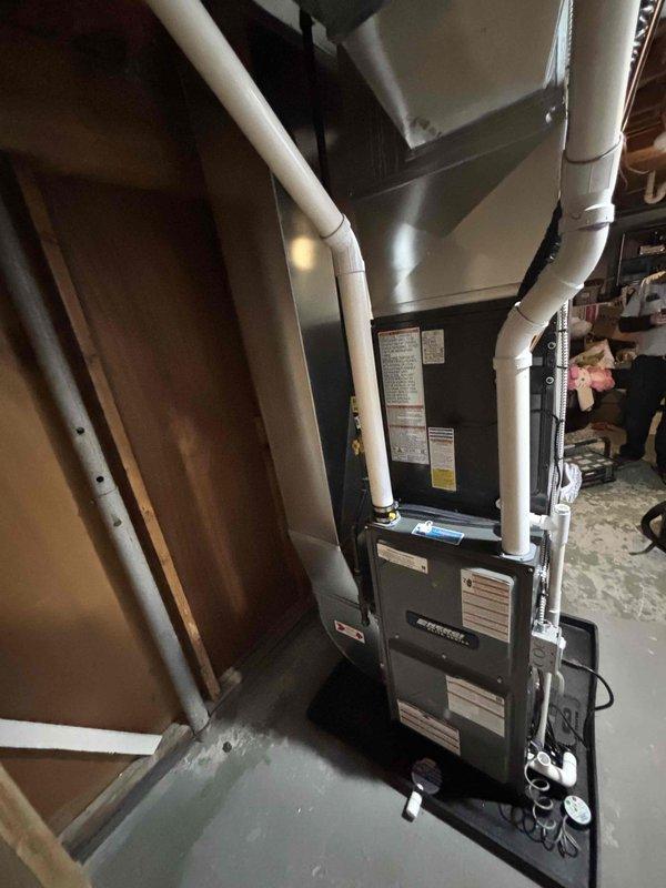 Completed installation of new Amana HVAC system including indoor furnace unit with PVC venting in utility area and outdoor AC condensing unit mounted on concrete pad. System properly connected to existing ductwork with all mechanical and electrical connections secured and tested for operation.