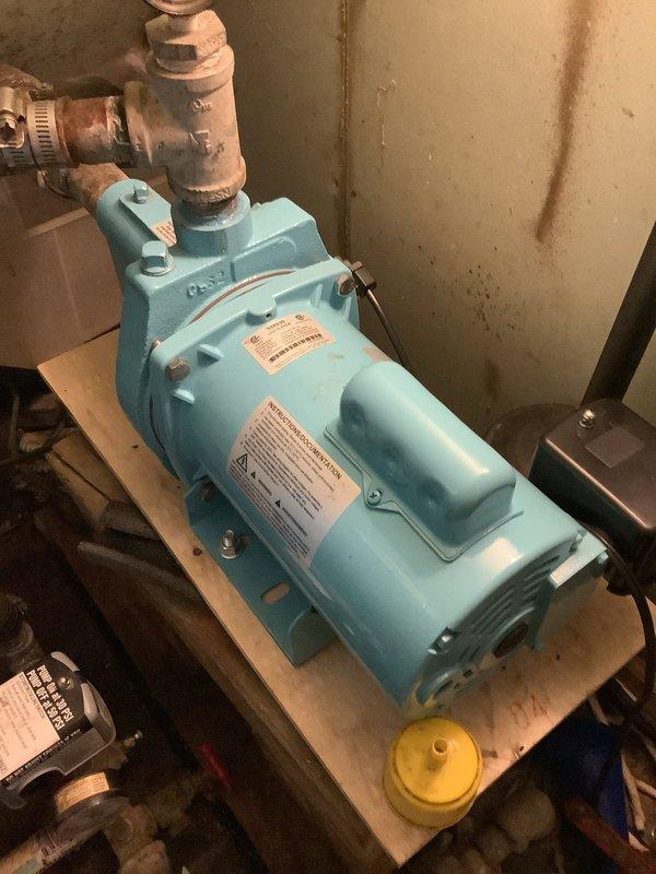 Diagnosed non-functioning sump pump located in basement utility area. Inspection revealed faulty motor in the light blue pump unit mounted on wooden platform, with visible corrosion at copper pipe connections. Replaced pump motor assembly, tested system functionality, and verified proper operation before completing service.