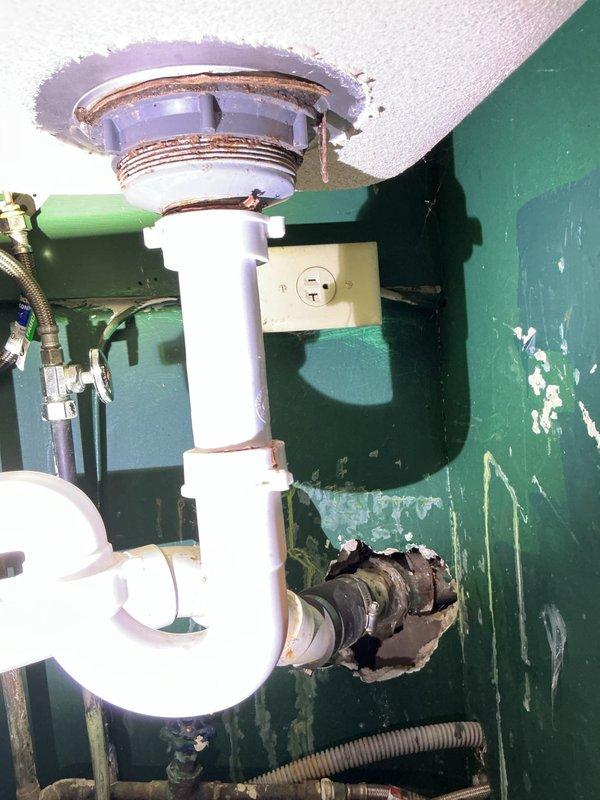 Diagnosed kitchen sink dual-basin drainage issue where water backed up into adjacent sink during drain use. Inspection revealed aged P-trap assembly with corrosion at sink connection and deteriorated wall area around drain exit point. Also identified leaking water supply valves at washer connection in basement requiring replacement.