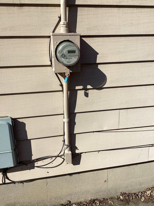 Completed site assessment for electrical panel upgrade. Inspected existing meter installation and electrical connections on exterior wall, documenting current setup with digital meter housed in gray metal enclosure mounted on vertical conduit. Evaluation confirmed need for panel upgrade as specified in work order.