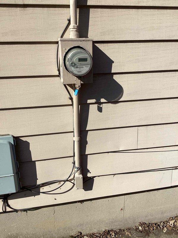 Completed site assessment for electrical panel upgrade. Inspected existing meter installation and electrical connections on exterior wall, documenting current setup with digital meter housed in gray metal enclosure mounted on vertical conduit. Evaluation confirmed need for panel upgrade as specified in work order.