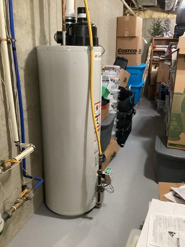 Conducted a water heater replacement estimate for a 14-year-old unit located in the basement utility area. Observed existing installation with copper plumbing connections and noted the surrounding environment including concrete walls and limited clearance due to storage items. Documented current configuration with photos to prepare comprehensive replacement options.