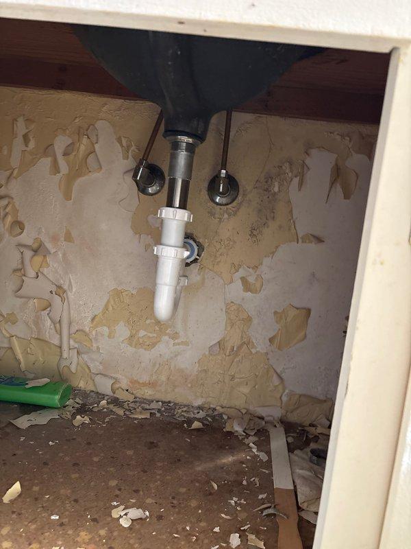 Responded to slow leak in 64-year-old home's bathroom sink present for approximately 3 days. Inspection revealed significant water damage to the cabinet and wall surrounding the drain assembly, with extensive deterioration of particleboard and drywall. Replaced damaged P-trap assembly and drain components, ensuring proper seals and connections to resolve the leak.