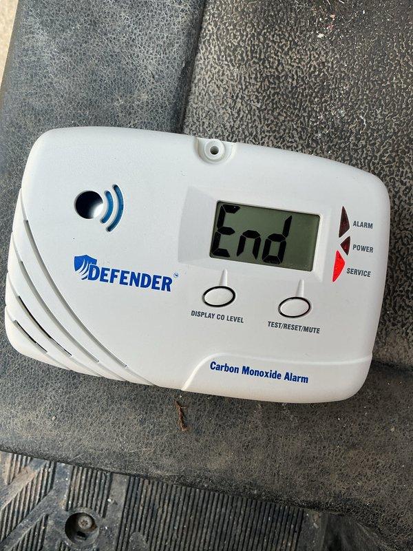 Responded to CO alarm activation for a visually impaired client. Upon inspection, found the Defender carbon monoxide detector displaying "End" message indicating end-of-life status. Replaced the expired unit with new detector which is now functioning properly, showing "0 PPM" reading. Client educated on proper CO alarm maintenance and replacement schedule.