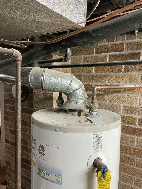 Conducted assessment of customer's GE water heater showing significant leakage requiring immediate replacement to prevent complete failure. Visual inspection confirmed active leaking from tank in this 1939 single-family residence. Documented current installation configuration with photos showing existing vent connections and plumbing setup to ensure proper replacement specifications.