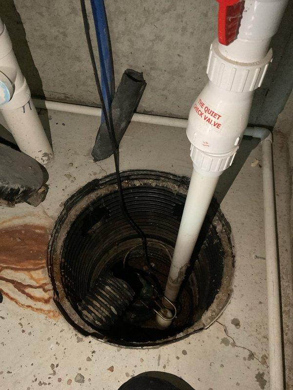 Conducted inspection of sump pump system in 8-year-old condo following home inspection concerns. Examined existing check valve installation and drainage configuration in basement utility area, documenting current condition with photos of the sump pit installation and associated plumbing infrastructure. Recommended possible replacement of LVM/Sample pump pending further assessment.