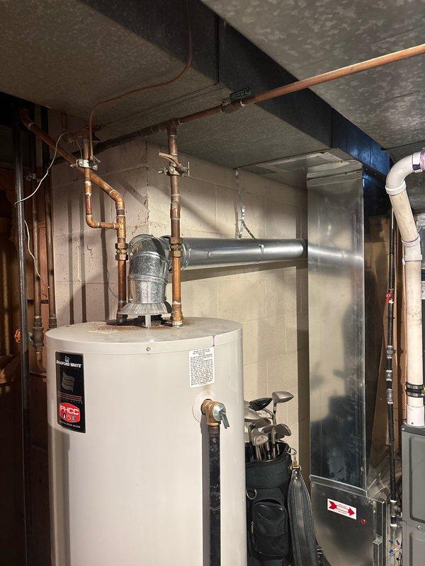 Conducted a comprehensive assessment of a 45-year-old residence for water heater replacement. Evaluated existing unit located in basement utility area, which features copper supply lines, brass valves, galvanized metal venting, and connections to home's plumbing system. Photos documented current installation configuration against concrete block walls for accurate replacement specifications.