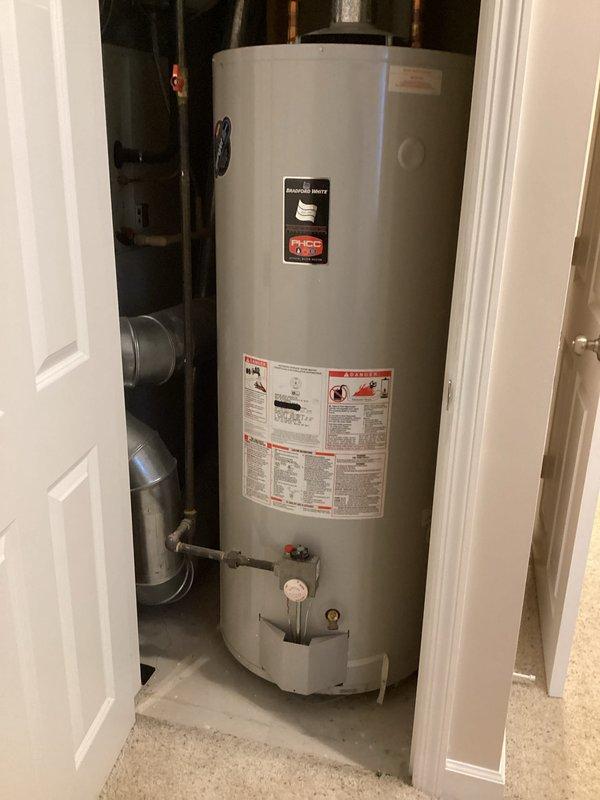 Performed inspection of 24-year-old water heater requiring replacement, located in confined utility space. Documented existing installation with photographs showing copper supply lines, ventilation, and current unit positioning. Provided customer with replacement options and information on Comfort Club membership, noting their plans for future HVAC system replacement.