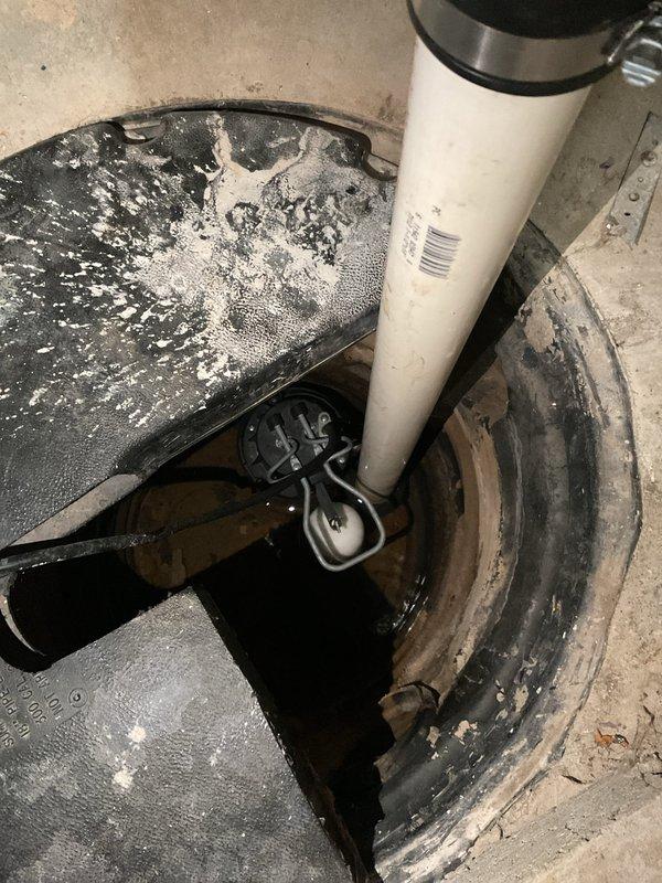 Performed estimate for backup sump pump installation in basement. Inspected existing sump pit containing standing water with visible float switch mechanism and documented current discharge plumbing configuration. Evaluated wall-mounted PVC discharge pipe system with installed check valve and noted signs of previous moisture issues requiring attention during potential installation.