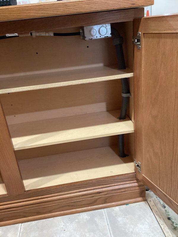 Completed subpanel relocation requiring concrete floor demolition to access and reroute existing electrical conduit. Removed cabinet shelving to accommodate new electrical junction box installation and properly secured conduit through cabinet interior for code compliance.