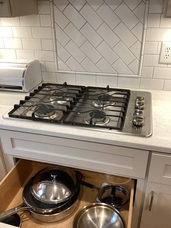 Conducted site assessment for gas cooktop installation and tankless water heater estimate. Inspected existing five-burner stainless steel cooktop integrated into white countertop with herringbone tile backsplash. Documented current kitchen configuration and appliance placement for accurate project planning and material requirements.