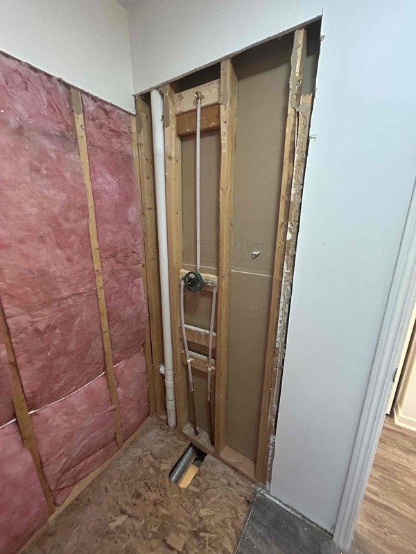 Completed Sterling shower installation with client valve assembly and CWOW. Successfully installed shower valve/mixing valve within wall cavity after accessing plumbing through opened wall with exposed studs. Project involved working around existing insulation and preparing the area for subsequent drywall finishing.