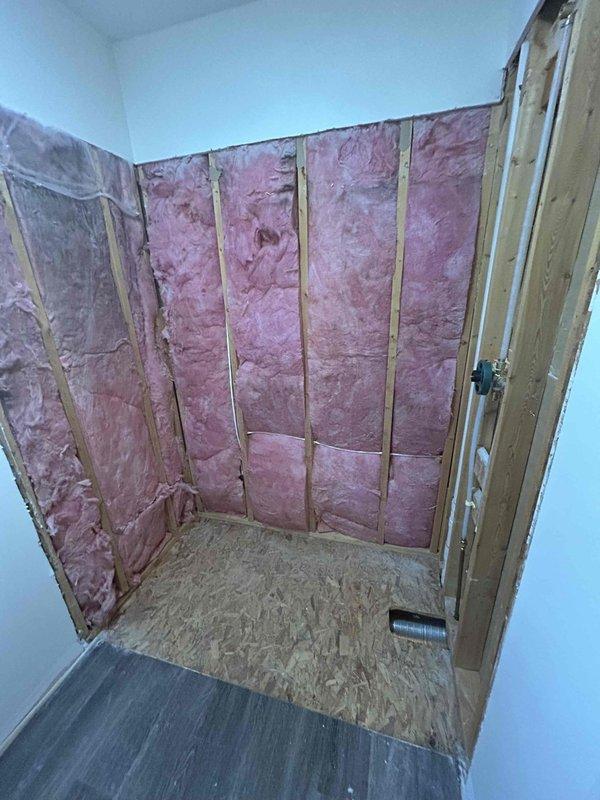 Completed Sterling shower installation with client valve assembly and CWOW. Successfully installed shower valve/mixing valve within wall cavity after accessing plumbing through opened wall with exposed studs. Project involved working around existing insulation and preparing the area for subsequent drywall finishing.