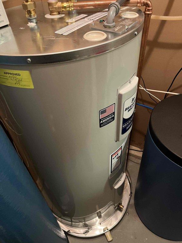 Installed correctly sized drain pan for water heater with adequate clearance between heater and pan edge. Connected temperature and pressure relief valve to drain properly into pan, and extended drain line from pan to existing floor drain as required per inspection correction.
