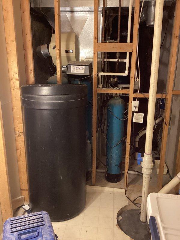 Inspected water conditioning system in utility area where customer reported leaking. Confirmed water softener tank is actively leaking at base, causing water damage to surrounding floor and wooden studs. Recommended complete replacement of water softener unit as repair is not economically viable given extent of deterioration.