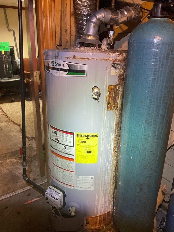 Performed complimentary annual furnace tune-up on 12-year-old Carrier system. Observed significant corrosion and rust on Smith water heater tank requiring attention, with deterioration visible at top surfaces, sides, and base. Noted secondary blue water treatment tank appears to be in better condition than primary unit.