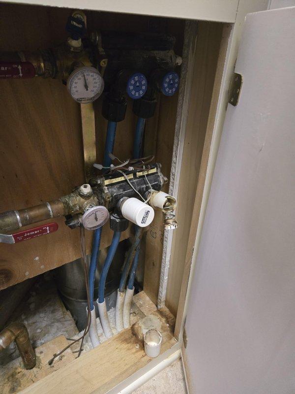 Diagnosed 28-year-old Slant Fin in-floor heating system that was non-operational. Inspected plumbing components including pressure gauges, valves, and copper pipe connections in the utility cabinet. System requires replacement due to advanced age and component deterioration evident in the pipe fittings and valve assemblies.