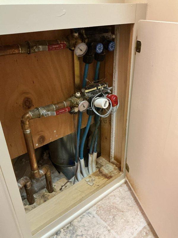 Diagnosed 28-year-old Slant Fin in-floor heating system that was non-operational. Inspected plumbing components including pressure gauges, valves, and copper pipe connections in the utility cabinet. System requires replacement due to advanced age and component deterioration evident in the pipe fittings and valve assemblies.