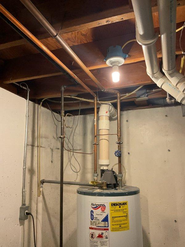 Responded to water leak complaint in basement area. Upon inspection, found significant water discharge from ceiling above Richmond PowerVent water heater, causing accumulation on basement floor. No visible damage to the water heater unit itself, which appears to be functioning normally. Documented current condition with photos showing the water heater installation and surrounding utility area with exposed joists.