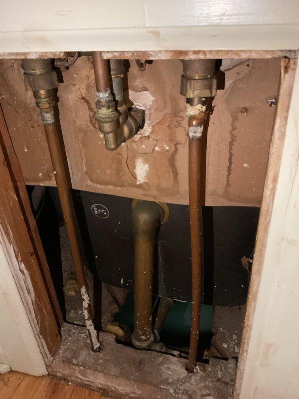 Repaired basement plumbing leak by replacing deteriorated clean-out elbow beneath bathtub that had developed a hole. Inspection revealed mineral deposits and corrosion at connection points, requiring removal of damaged wall material to access and properly seal the affected plumbing components.