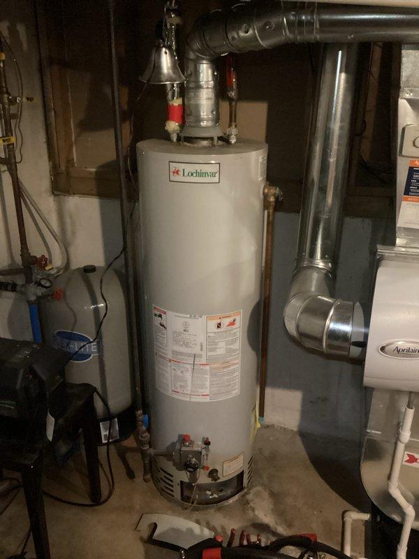 Completed assessment for replacement of 30-year-old propane-fueled tank water heater for family of 6 with two full bathrooms in 30-year-old home. Documented existing Lochinvar water heater installation with associated plumbing connections and ventilation system. Took photos of current setup including the water heater and adjacent HVAC system to facilitate proper sizing and installation requirements for the replacement unit.