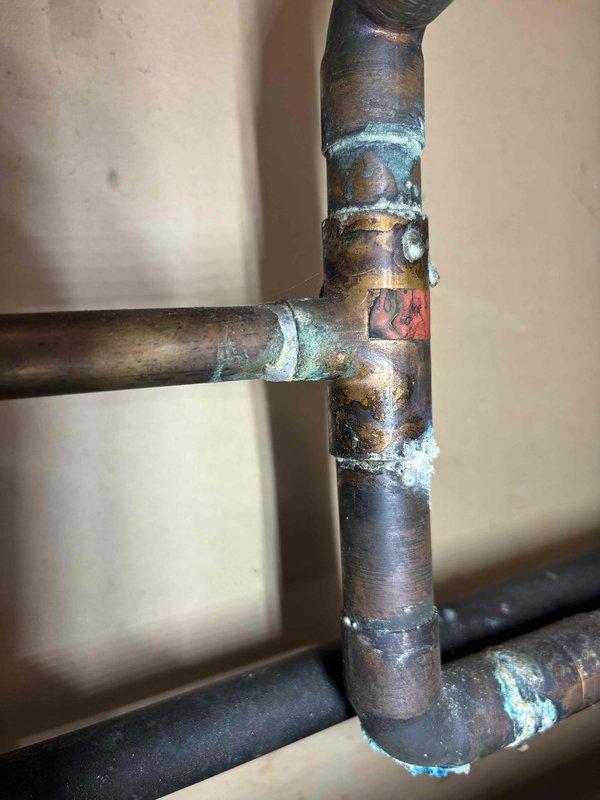 Responded to water leak report for new Bradford White water heater (model WT 10-2026). Inspection revealed leakage at the top near a plastic cap, originating from improperly soldered copper pipe connections. Repaired the faulty T-junction joint and verified proper operation with no further leakage.