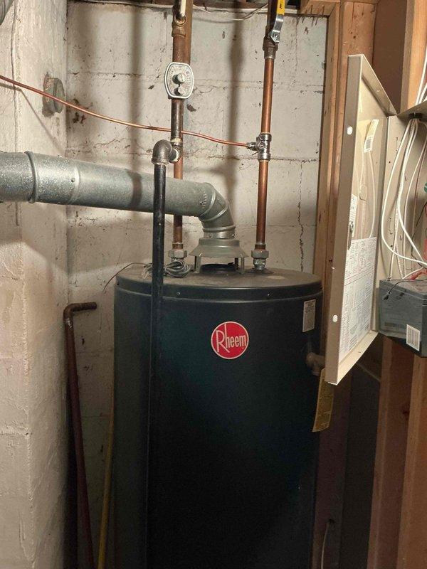 Conducted on-site assessment for toilet installation estimate in a 50-year-old single-family home. Inspected existing Rheem water heater installation in basement utility area, noting proper copper pipe connections, functional vent pipe, and pressure gauge. Documentation photos taken of water heater system to provide comprehensive estimate for requested plumbing project.