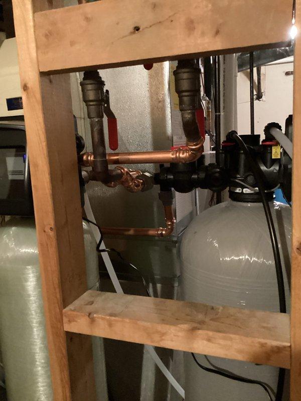 Completed installation of a water softener system in utility area with proper connection to existing plumbing infrastructure. Successfully integrated the gray cylindrical treatment tank with black valve assembly into the home's water system using appropriate PVC piping and fittings. System was properly secured and tested to ensure optimal functionality.