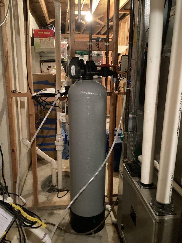 Completed installation of a water softener system in utility area with proper connection to existing plumbing infrastructure. Successfully integrated the gray cylindrical treatment tank with black valve assembly into the home's water system using appropriate PVC piping and fittings. System was properly secured and tested to ensure optimal functionality.