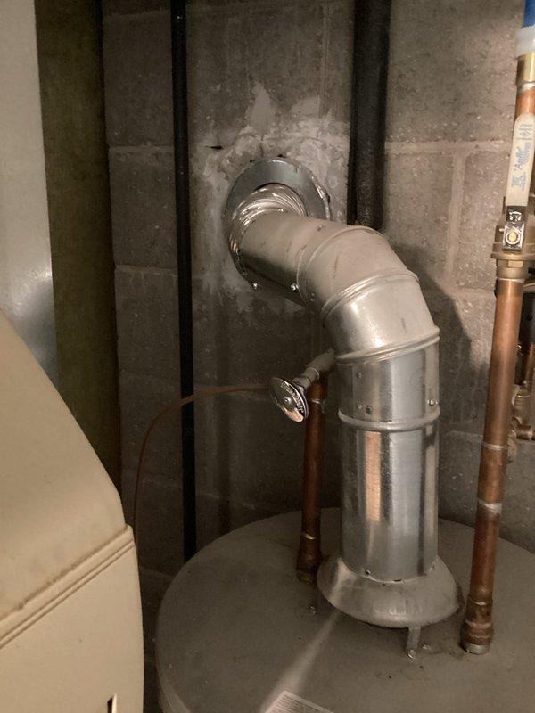 Diagnosed 14-year-old Bradford White water heater that was not lighting. Inspected vent pipe configuration and exhaust system through concrete block wall, noting signs of previous repairs around wall penetration. Resolved ignition issue and verified proper operation of the Defender water heater unit before completing service.