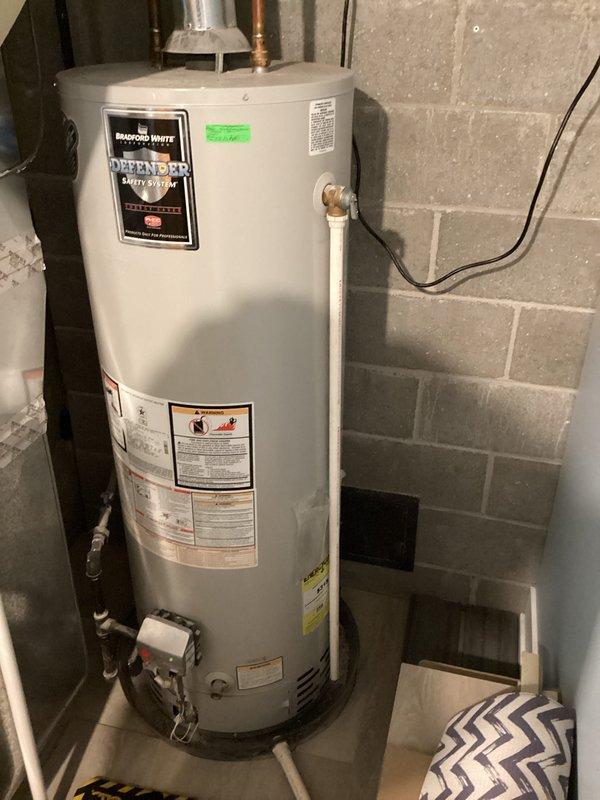 Diagnosed 14-year-old Bradford White water heater that was not lighting. Inspected vent pipe configuration and exhaust system through concrete block wall, noting signs of previous repairs around wall penetration. Resolved ignition issue and verified proper operation of the Defender water heater unit before completing service.