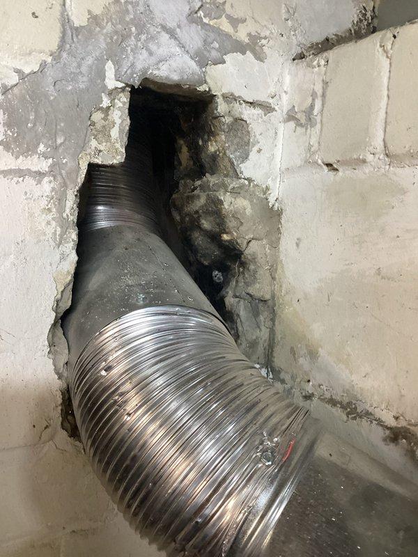 Completed annual heating maintenance on 20-year-old Nordyne furnace with no humidifier. Inspected flexible aluminum ductwork that passes through a damaged concrete wall opening, noting deterioration around the unfinished hole. Examined system components including water heater connections and galvanized sheet metal ducting. Took documentation photos of the installation for service records.