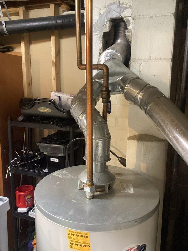 Completed annual heating maintenance on 20-year-old Nordyne furnace with no humidifier. Inspected flexible aluminum ductwork that passes through a damaged concrete wall opening, noting deterioration around the unfinished hole. Examined system components including water heater connections and galvanized sheet metal ducting. Took documentation photos of the installation for service records.