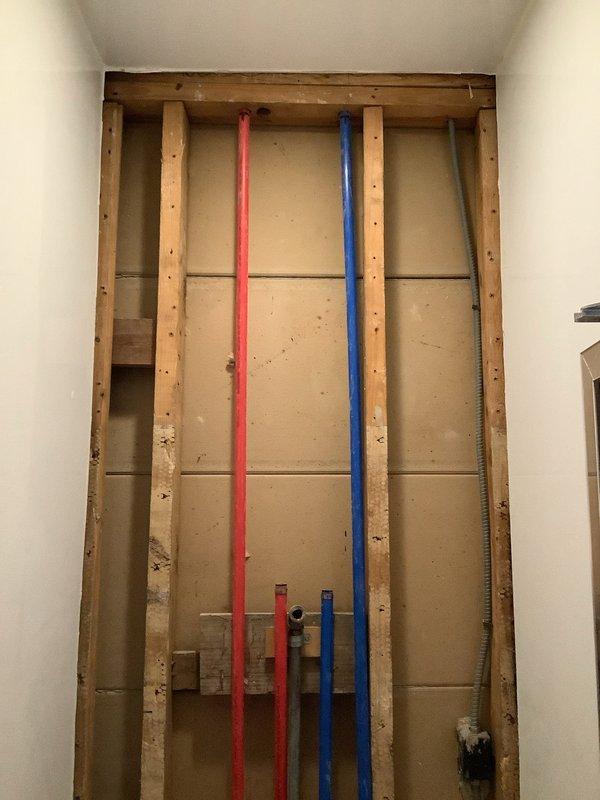 Performed inspection of exposed wall cavity to assess single shower plumbing system in 75-year-old home. Documentation shows PEX hot and cold water lines (red and blue) properly secured within wooden framing, with visible drain connections at shower pan. Photos were taken of the exposed plumbing configuration to assist with replacement/repair estimate.