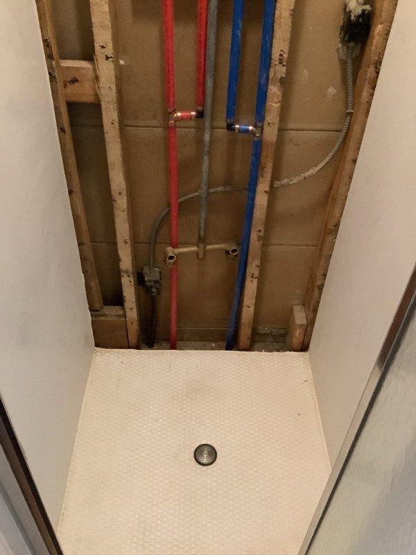 Performed inspection of exposed wall cavity to assess single shower plumbing system in 75-year-old home. Documentation shows PEX hot and cold water lines (red and blue) properly secured within wooden framing, with visible drain connections at shower pan. Photos were taken of the exposed plumbing configuration to assist with replacement/repair estimate.