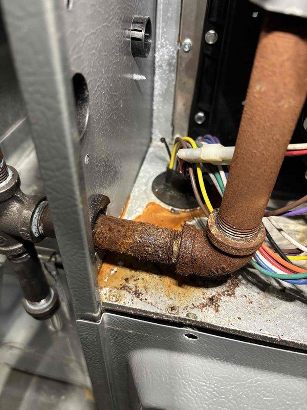 Diagnosed water leak on 11-year-old Daikin furnace system; inspection revealed severe corrosion and rust on copper pipe elbow fitting causing water to leak onto mounting panel. Documentation with photos shows extensive rust damage and moisture accumulation in the equipment housing.