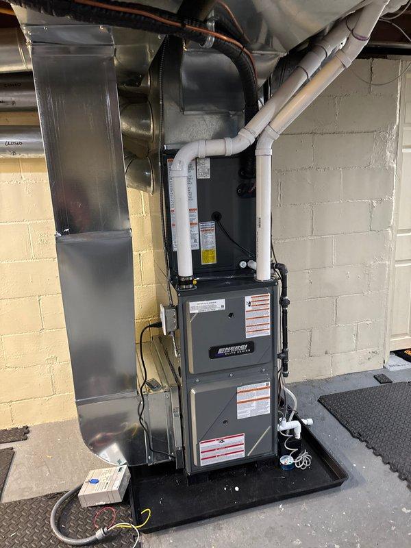 Successfully completed installation of new HVAC system in basement utility area, including furnace mounted on protective composite pad with proper electrical connections. System includes complete ductwork installation with metal cylindrical ducts and PVC ventilation pipes, all properly secured and connected according to manufacturer specifications.