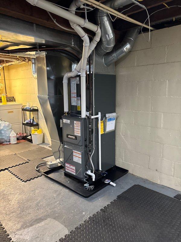 Successfully completed installation of new HVAC system in basement utility area, including furnace mounted on protective composite pad with proper electrical connections. System includes complete ductwork installation with metal cylindrical ducts and PVC ventilation pipes, all properly secured and connected according to manufacturer specifications.