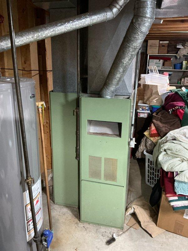 Conducted comprehensive assessment of 16-year-old furnace system and property for potential replacement and AC addition. Observed aging mint-green furnace unit with existing ductwork in basement utility area. Documented current installation configuration including ventilation connections and available space for new equipment to prepare accurate system replacement and AC installation quote.