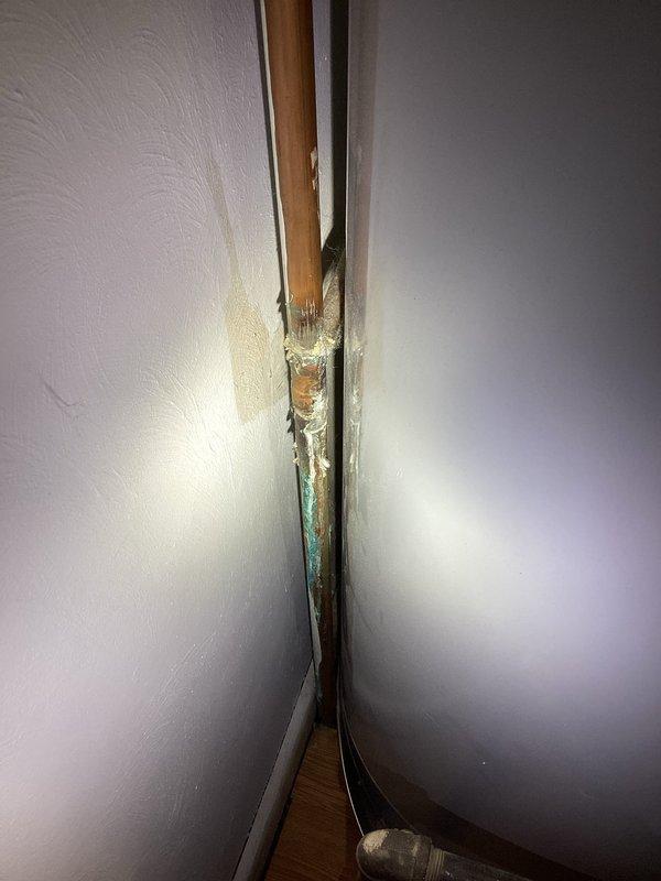 Identified and repaired a pinhole leak in copper piping at corner wall junction that was causing significant water damage and pipe corrosion. Removed deteriorated section of copper pipe showing extensive greenish oxidation and replaced affected plumbing components to resolve persistent leak that was previously misdiagnosed.